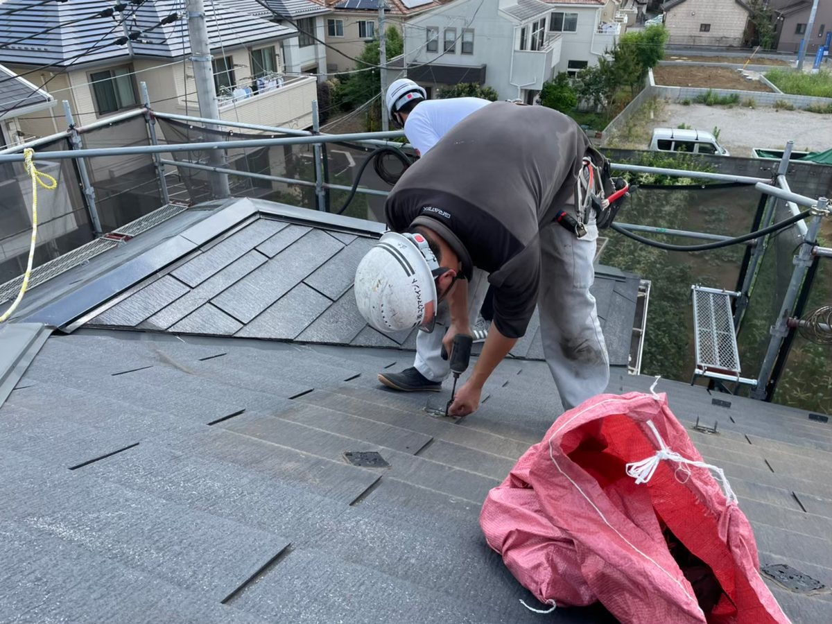 スレート屋根の上で屋根材を固定する職人